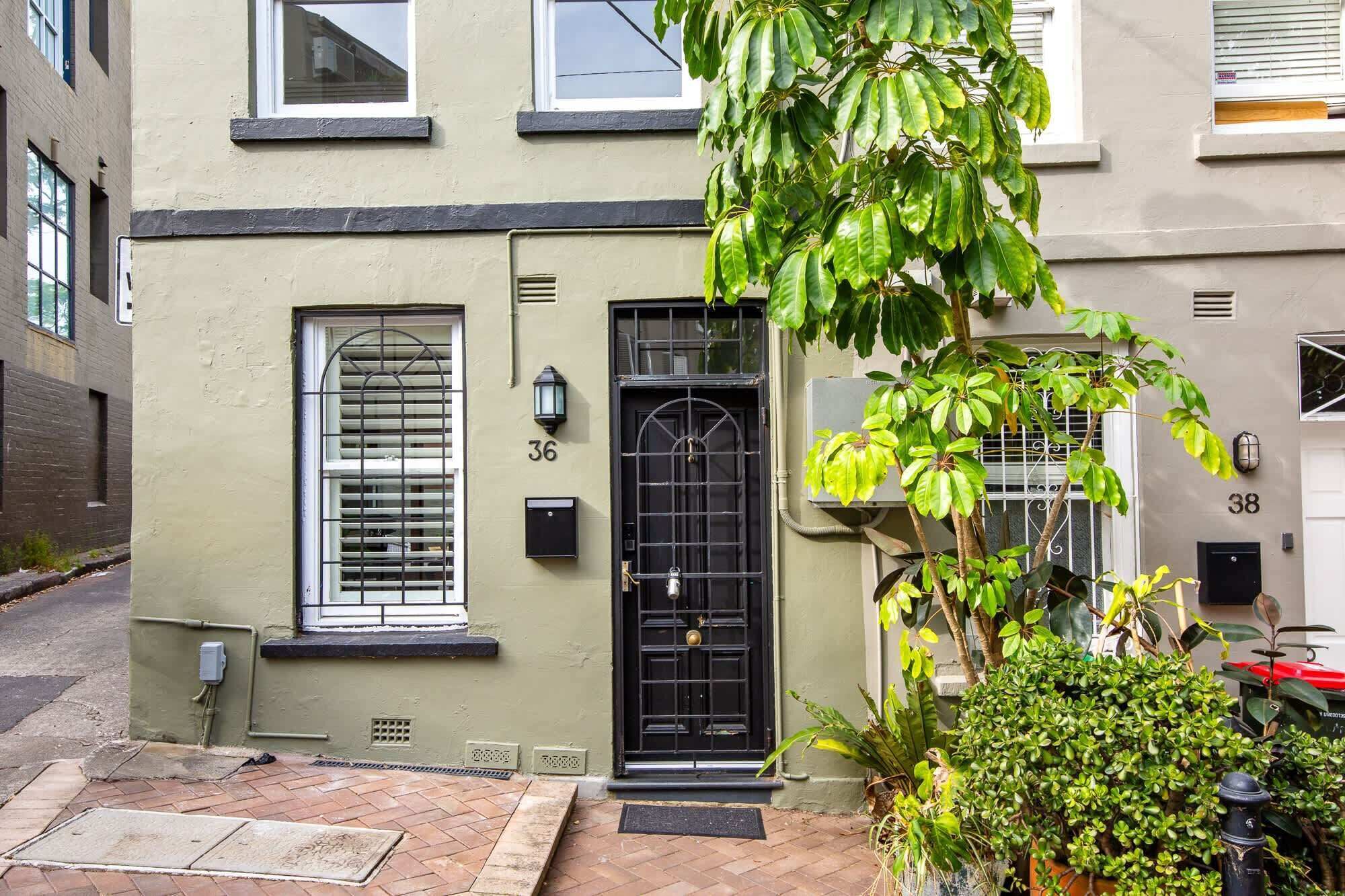 A townhouse with a black front door, a window with blinds, and a small porch area.