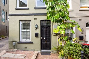 Une maison de ville avec une porte d’entrée noire, une fenêtre avec des stores et un petit porche.