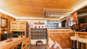 A rustic kitchen with wooden cabinets, a bar area, and a dining table with chairs. - Charming Alpine guesthouse for 23 people (Hollersbach im Pinzgau)
