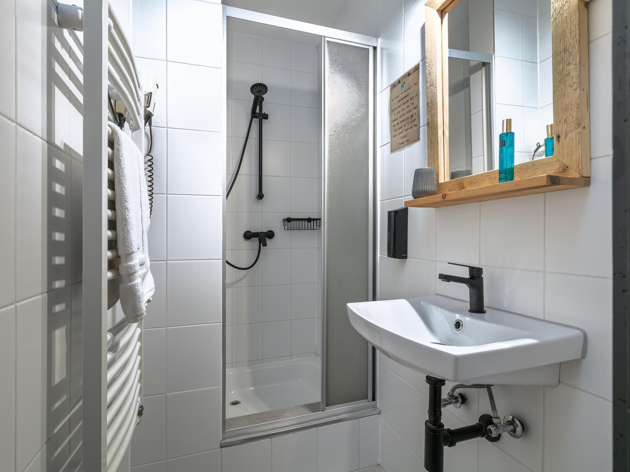 A modern bathroom with a glass shower enclosure, a white sink, and a wooden shelf with toiletries.