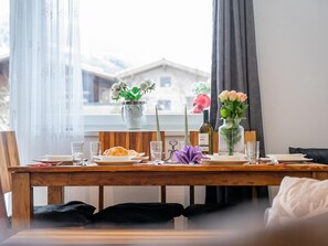 A dining table set with plates, glasses, and a bottle, with a window view of a building and a vase with flowers. - Cosy holiday apartment in Bramberg (Bramberg)
