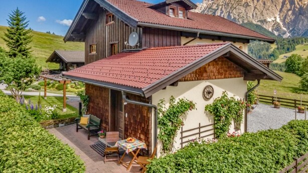 Eine Chalet mit rotem Ziegeldach, Holzfassade und einer Terrasse mit Gartenmöbeln.