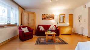 Ein gemütliches Wohnzimmer mit einem roten Sofa, einem Holztisch und einer Holzkommode.