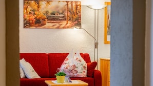 Ein Wohnzimmer mit einem roten Sofa, einem kleinen Holztisch mit einer Pflanze und einem Bild an der Wand.