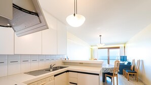 A modern kitchen with white cabinets, a dishwasher, and a stove. There is a dining area with a table and chairs, and a view of the sea through large windows. - Apartment on the 6th floor with sea view (Middelkerke)
