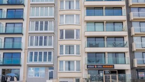 En flervåningsbyggnad med bostäder och balkonger, en butikslokal på markplan och en synlig soptunna.