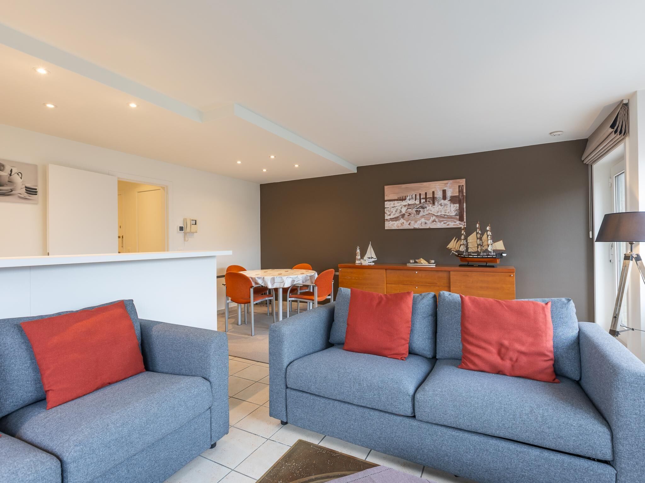 A modern living room with two grey sofas, a wooden dining table, and a small ship model on the wall.