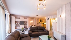 A modern living room with a sectional sofa, a glass coffee table, and a built-in kitchen in the background. - Apartment with 2 bedrooms and large terrace (Middelkerke)