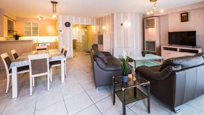 A modern living room with a dining area, a sofa set, a TV, and a glass coffee table. - Apartment with 2 bedrooms and large terrace (Middelkerke)