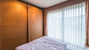 A hotel room with a large bed, wooden paneling on the walls, and a large window with sheer curtains. - Apartment with 2 bedrooms and large terrace (Middelkerke)