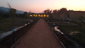 Un sendero conduce a un edificio con ventanas iluminadas, rodeado de agua y vegetación.