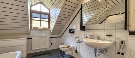 A modern bathroom with a sloped ceiling, a large window, a bathtub, a toilet, and a sink.