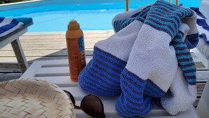 A poolside area with a lounge chair, a bottle, and a towel.