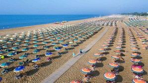 A beach with rows of umbrellas and sun loungers, a clear sky, and the ocean in the background. - Holiday flat with air conditioning and balcony (Bibione)