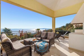 A balcony with wicker furniture, a table with a plate of fruit, and a view of the sea. - Holiday home with pool and sea view (Poljane)