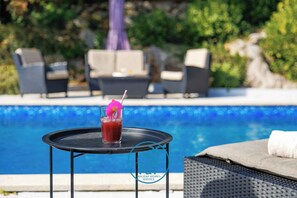 Ein Poolbereich mit Tisch, Getränk und Liegestühlen.