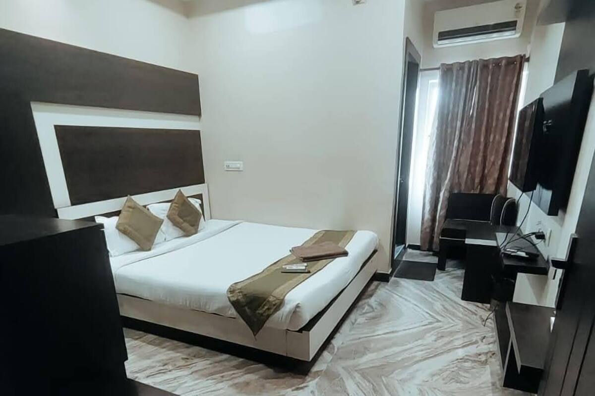A modern bedroom with a large bed, a flat-screen TV, a desk, and an air conditioning unit.