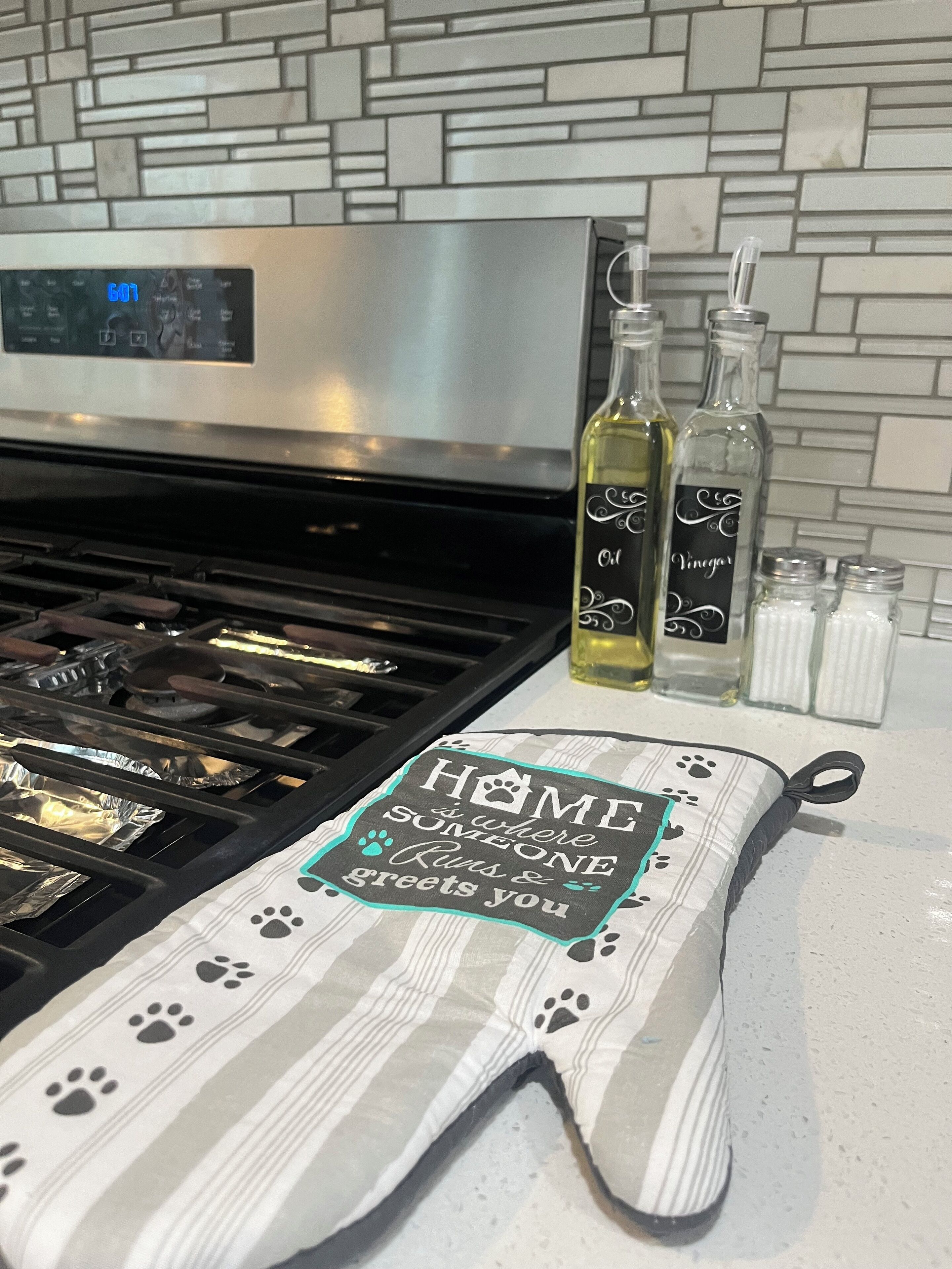 A kitchen with a stainless steel stove, a digital clock, and bottles of olive oil and vinegar on the counter.