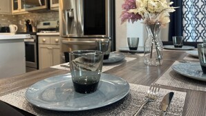 A modern kitchen with stainless steel appliances, a dining table set with plates, glasses, and cutlery. - Spacious 4-bedroom house in charming Newark with AC (Newark)
