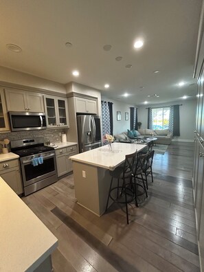 A modern kitchen with stainless steel appliances, a central island with bar stools, and a view to a living area. - Spacious 4-bedroom house in charming Newark with AC (Newark)