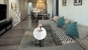 A modern living room with a sofa, coffee table, and TV. There is a dining area in the background with a kitchen visible. - Spacious 4-bedroom house in charming Newark with AC (Newark)