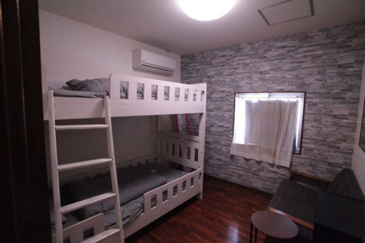 A bunk bed room with a stone wall, a window with curtains, and a small table.