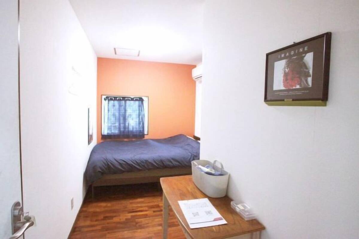 A small room with a bed, a desk, a chair, a window with curtains, and a framed picture on the wall.