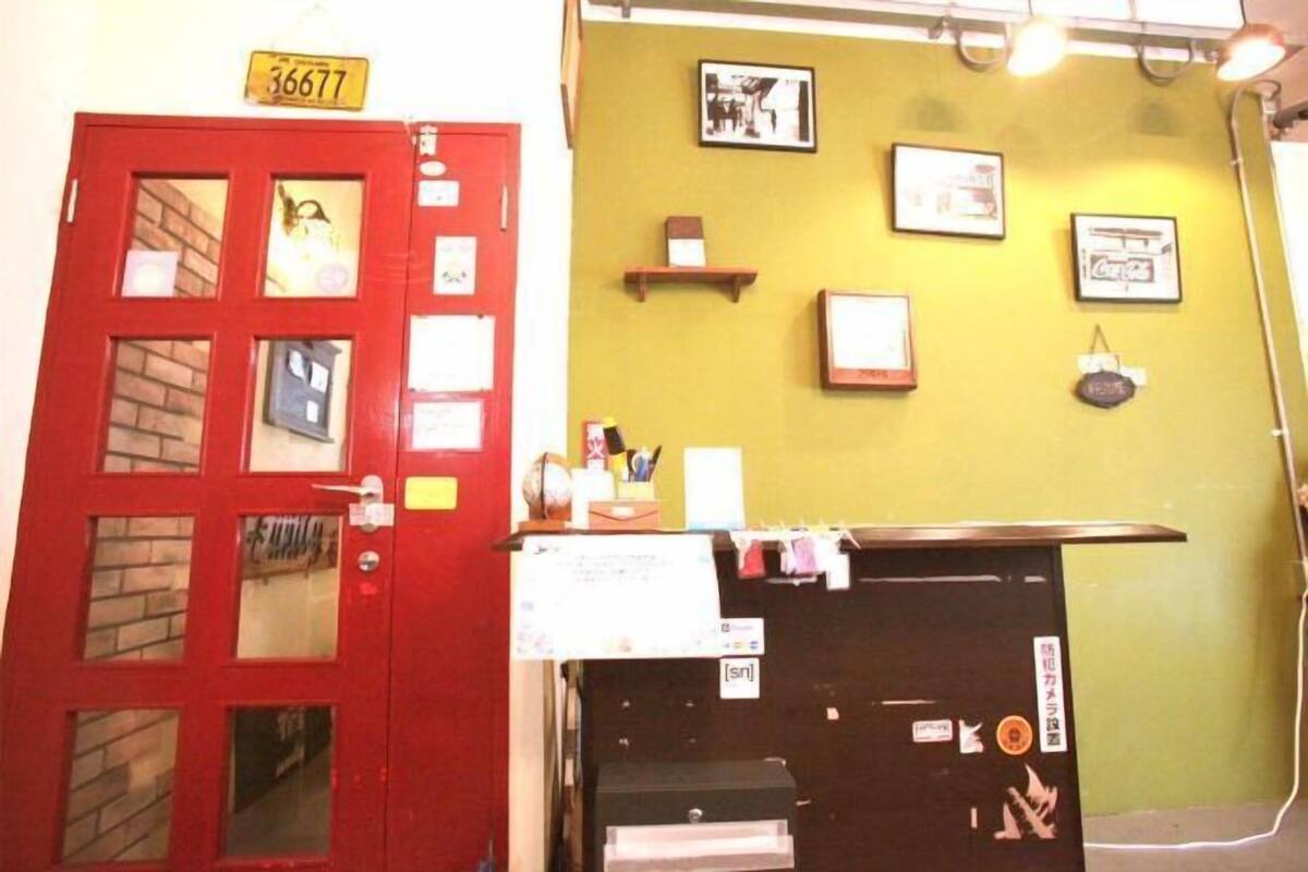 A red door with a number sign, a bulletin board, and framed pictures on a yellow wall.