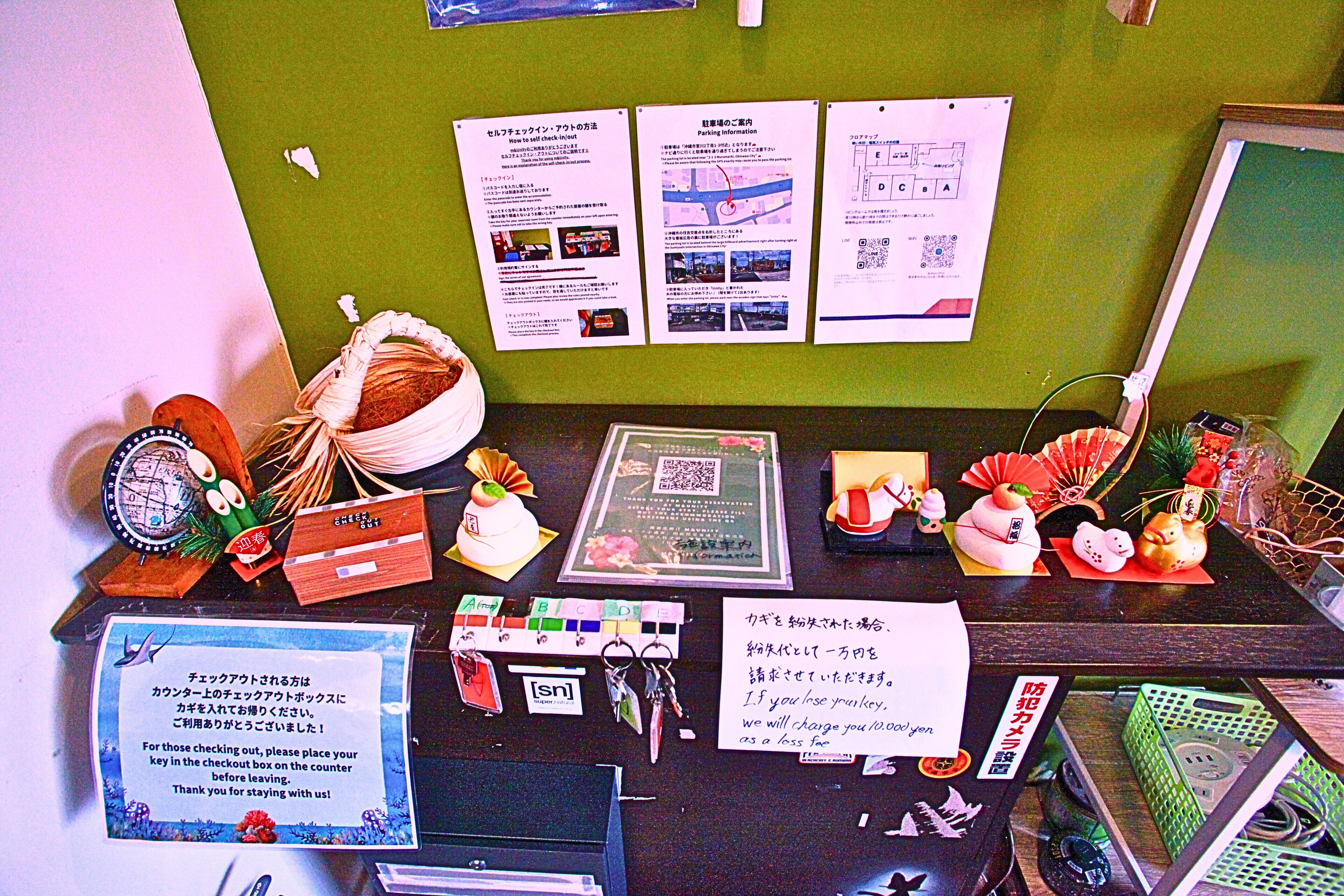 A counter with various informational posters, a QR code, and a sign instructing customers to place their keys in the checkout box.