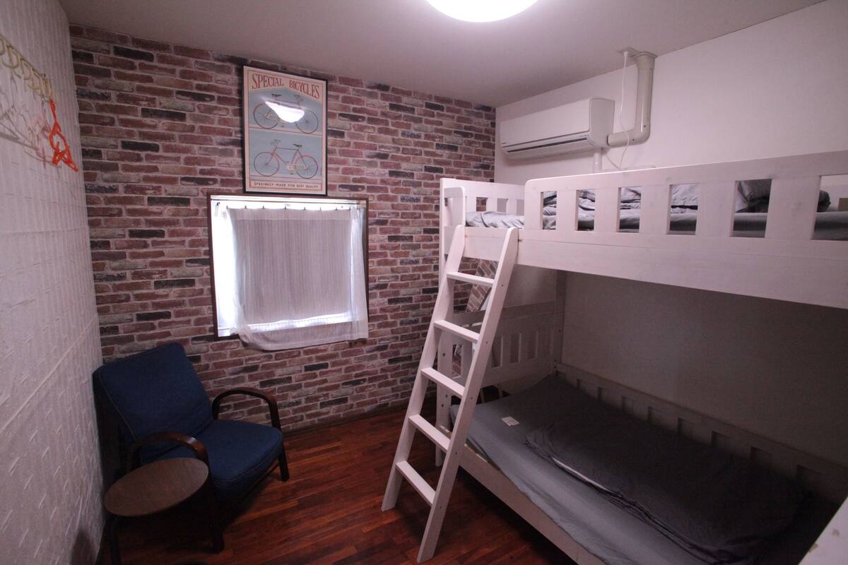 A room with a brick wall, a bunk bed, a blue chair, and a ladder.