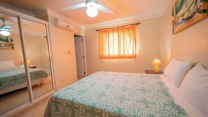 A bedroom with a bed, a ceiling fan, a window with curtains, a bedside lamp, and a door leading to another room. - Silent residence in downtown Sosua, you don't hear that every day! (Sosúa)