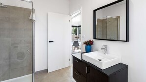 Ein modernes Badezimmer mit Duschkabine aus Glas, einem weißen Waschbecken mit schwarzem Unterschrank und einem großen Spiegel an der Wand.