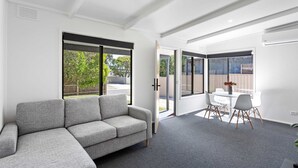 Ein modernes Wohnzimmer mit einem grauen Ecksofa, einem Esstisch mit Stühlen und großen Fenstern mit Blick ins Freie.