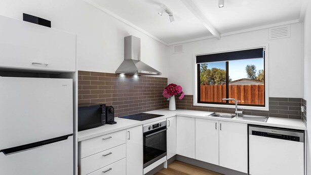 Eine moderne Küche mit weißen Schränken, einem eingebauten Backofen, einer Spülmaschine und einem Fenster mit Ausblick.