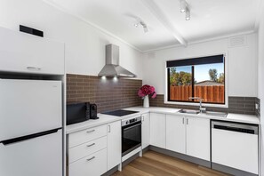 Una cocina moderna con armarios blancos, horno integrado, lavavajillas y ventana con vistas al exterior.