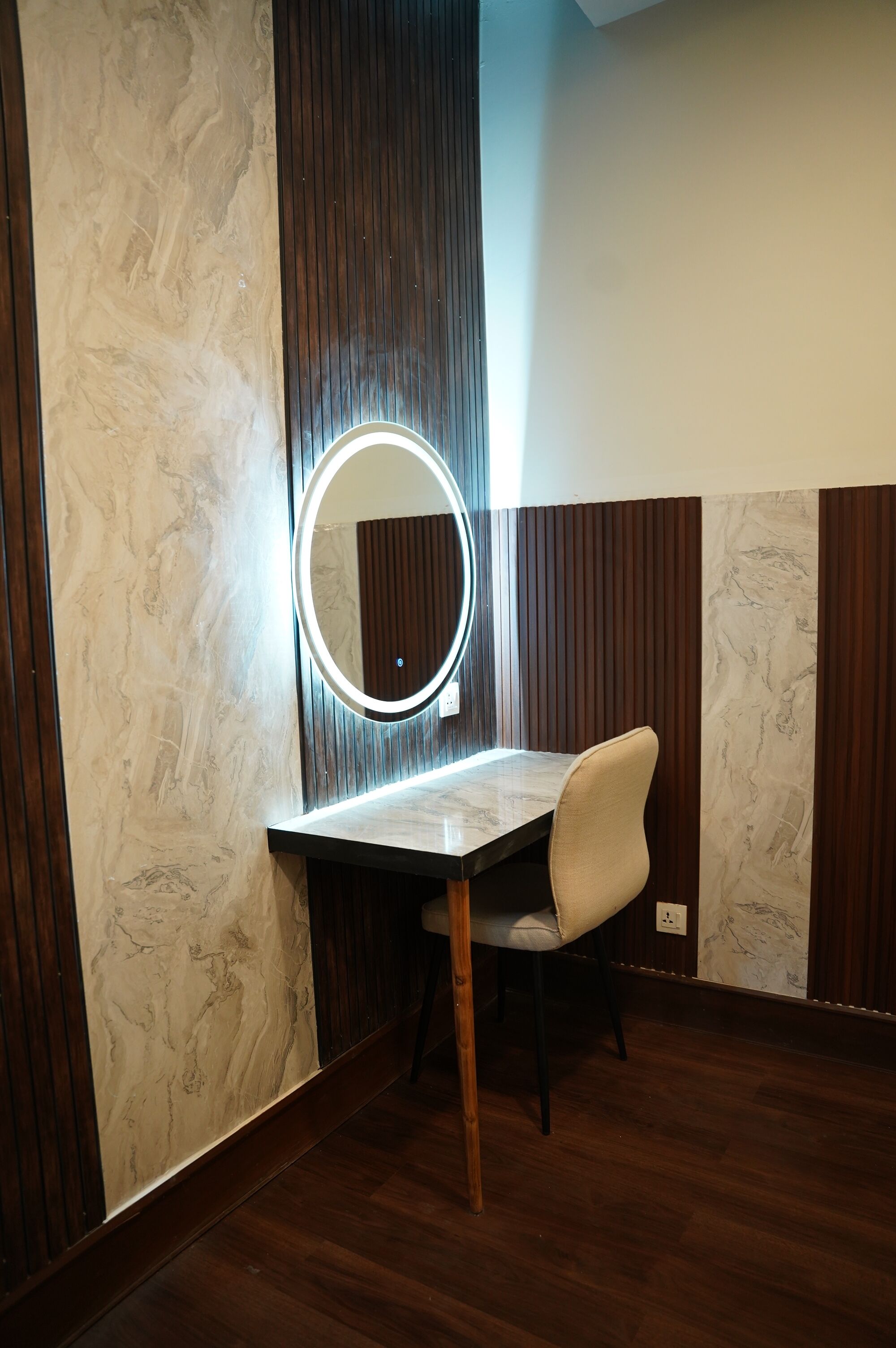 A vanity with a mirror and light, a chair, and wooden paneling on the walls.