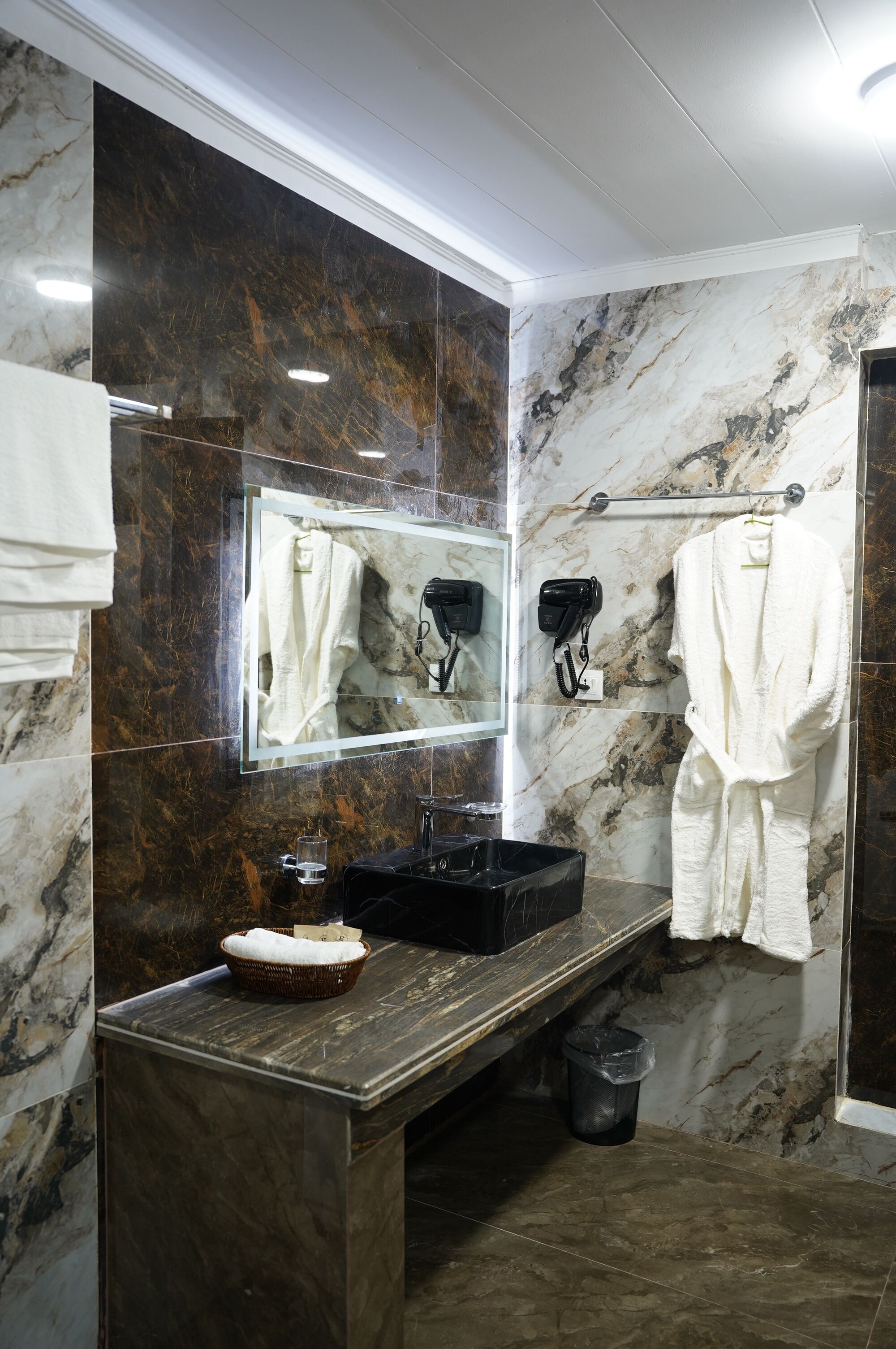 Un bagno con parete in marmo, uno specchio, un lavandino, un portascopino e un accappatoio appeso al muro.