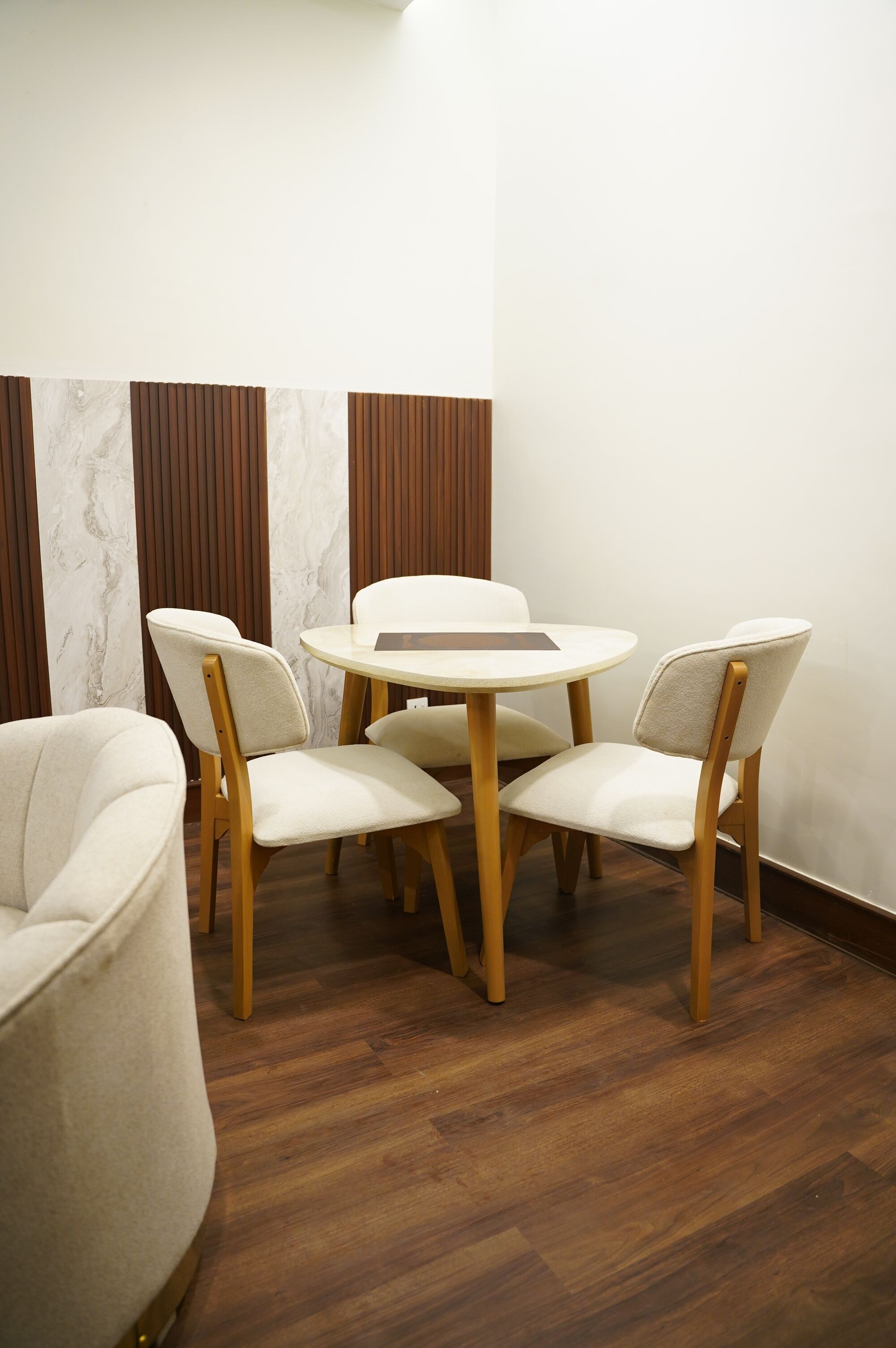 Un comedor con una mesa redonda y cuatro sillas, suelo de madera y una pared blanca con listones verticales de madera.