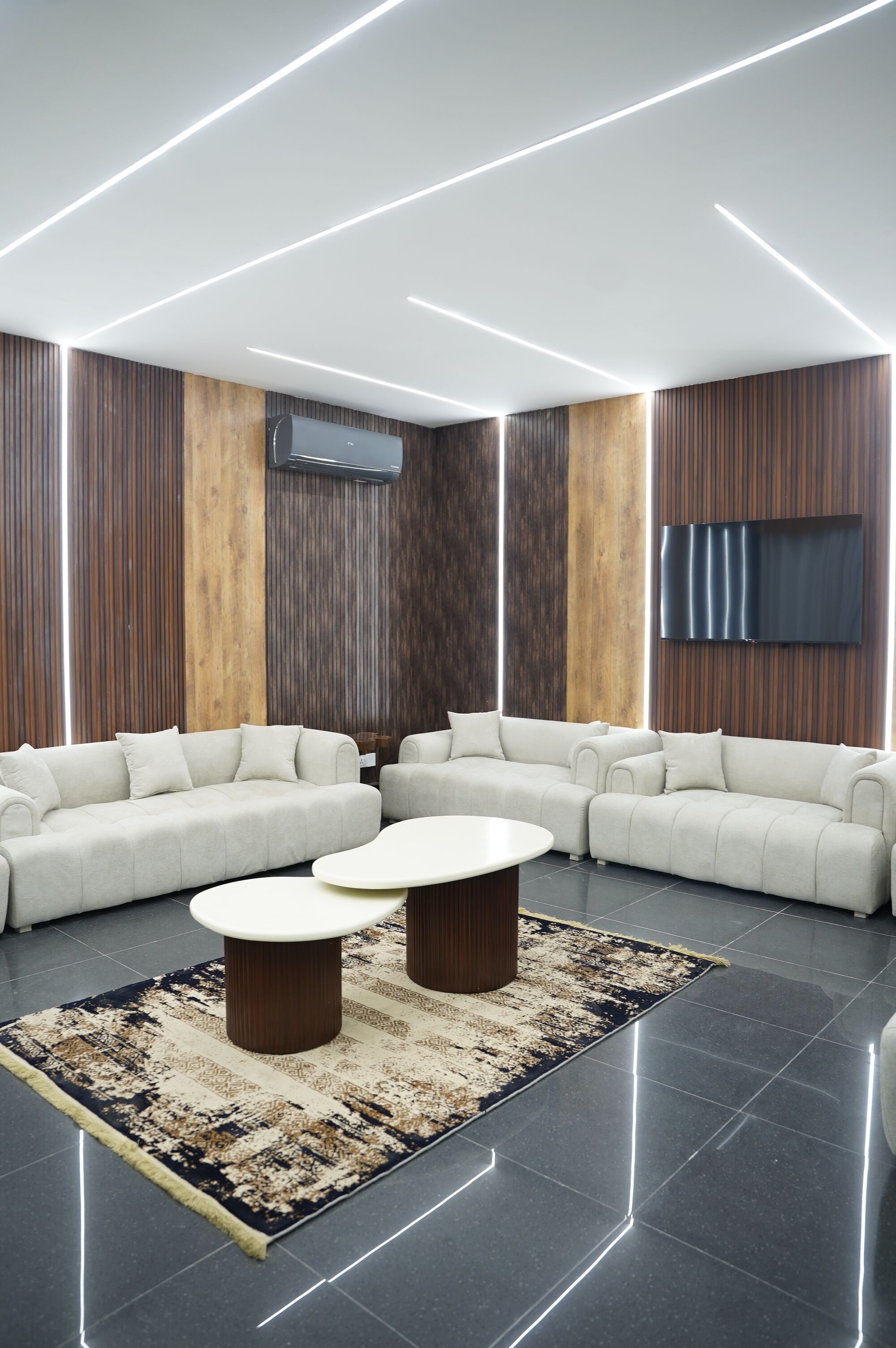 A modern living room with a sectional sofa, two round coffee tables, and a large flat-screen TV mounted on the wall.
