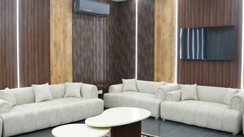A modern living room with a sectional sofa, two round coffee tables, and a large flat-screen TV mounted on the wall.