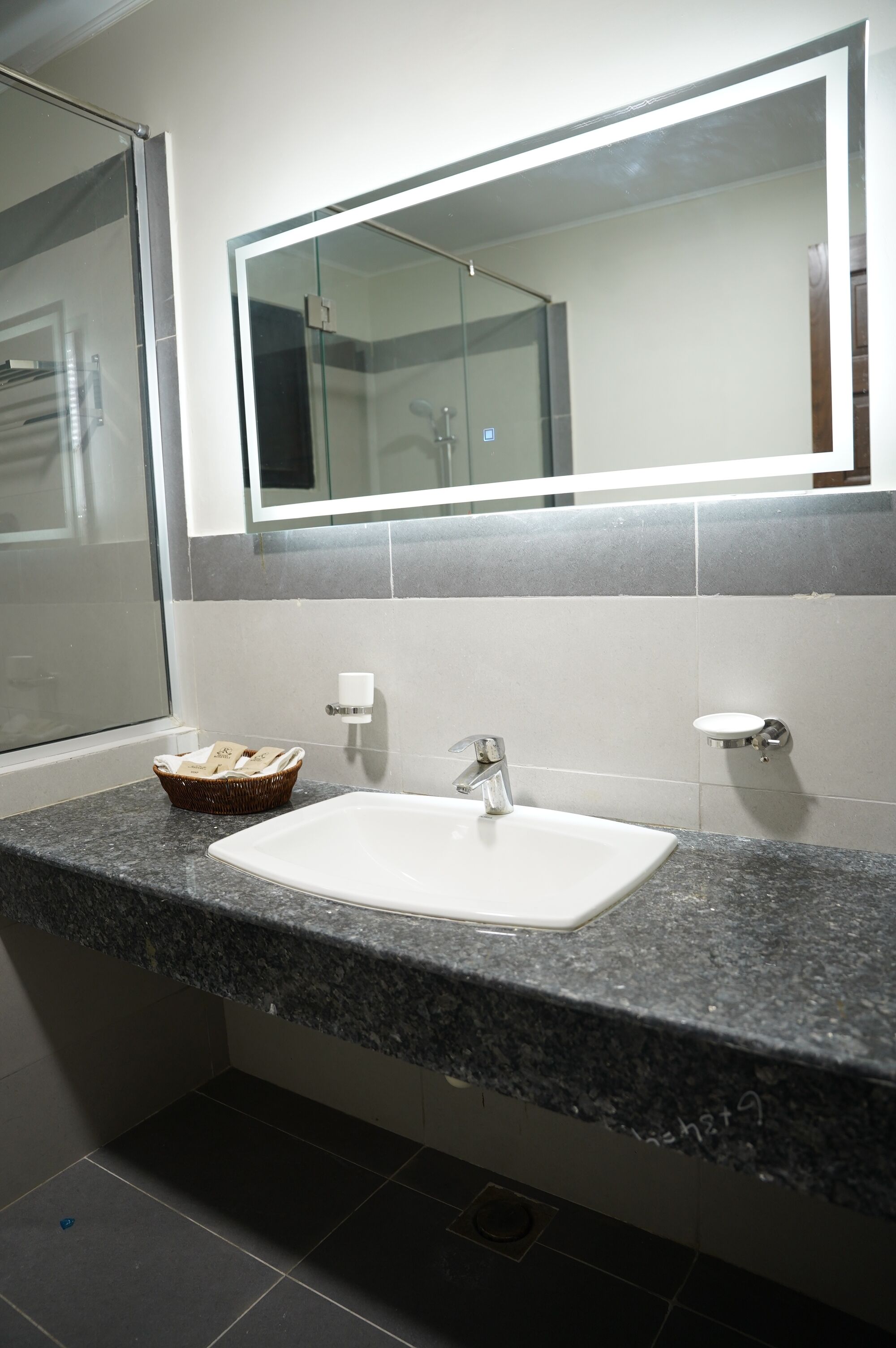A bathroom with a granite countertop, a white sink, a mirror, and a basket of toiletries.