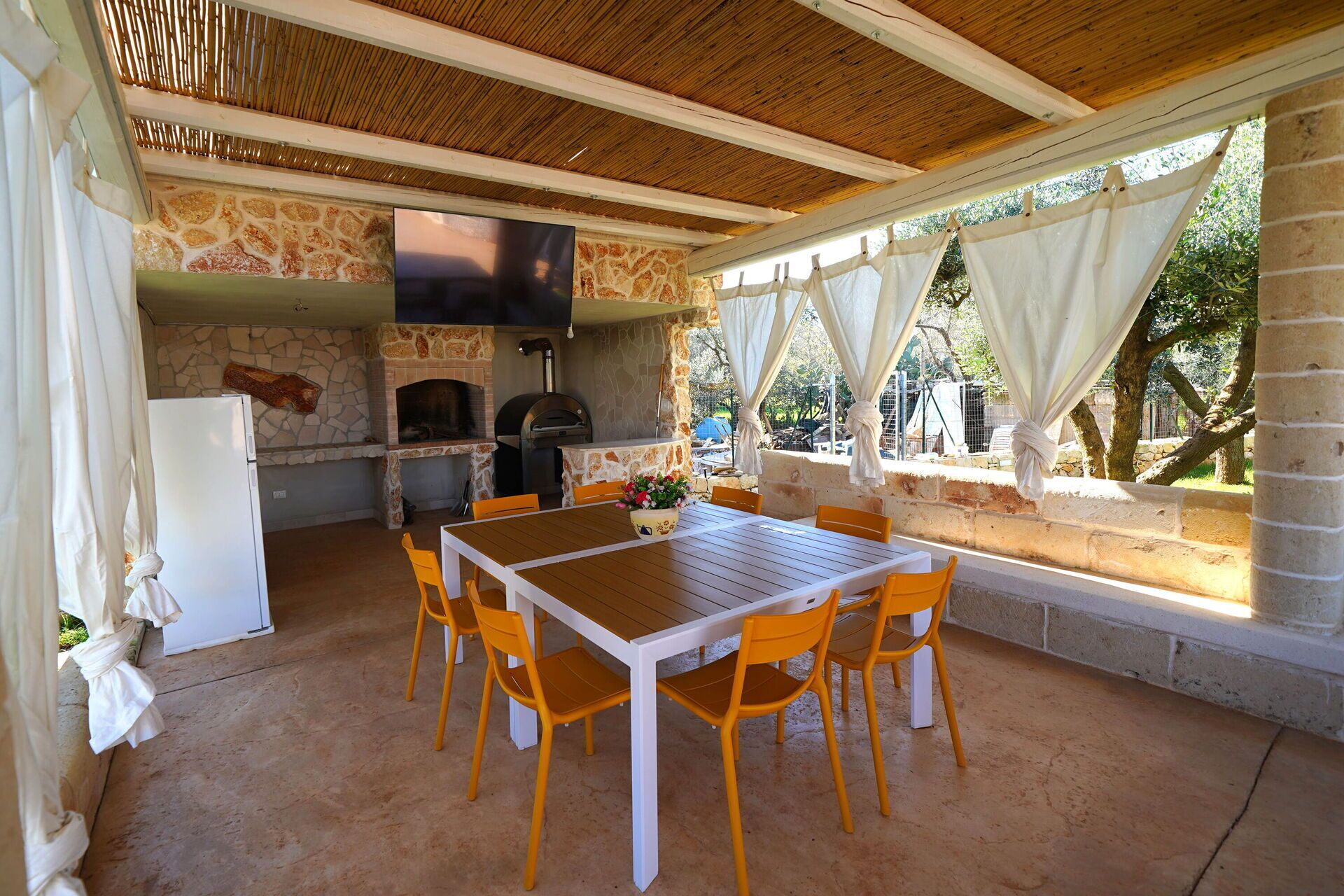 A covered outdoor dining area with stone walls, a stone fireplace, and a grill.