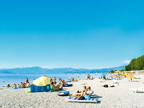A pebble beach with people sunbathing, swimming, and using inflatable floats. - Nice apartment in villa for 6 guests with pool, WIFI, A/C, terrace and pets allowed (Peschiera Del Garda)