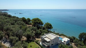 Una moderna casa a due piani con piscina, immersa nel verde e affacciata su un mare calmo.