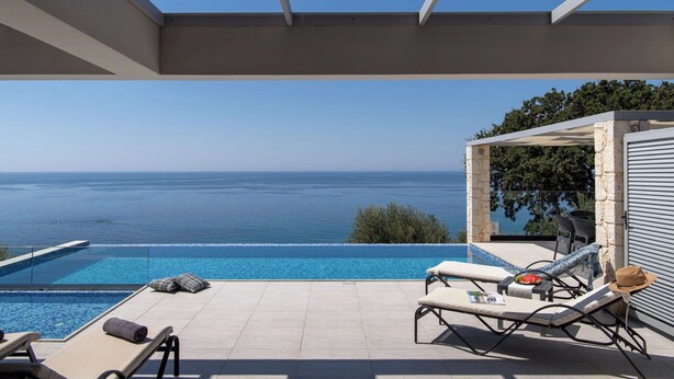 Area a bordo piscina con vista libera sul mare, sedie a sdraio e una zona salotto coperta.