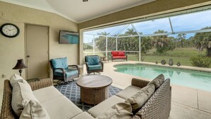 A poolside area with wicker furniture, a clock, and a TV on the wall. - Beach Days & Fairways: Rotonda West Snowbird Home (Rotonda West)