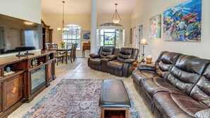 A spacious living room with a leather sofa, a dining area with a chandelier, and a large painting on the wall. - Beach Days & Fairways: Rotonda West Snowbird Home (Rotonda West)