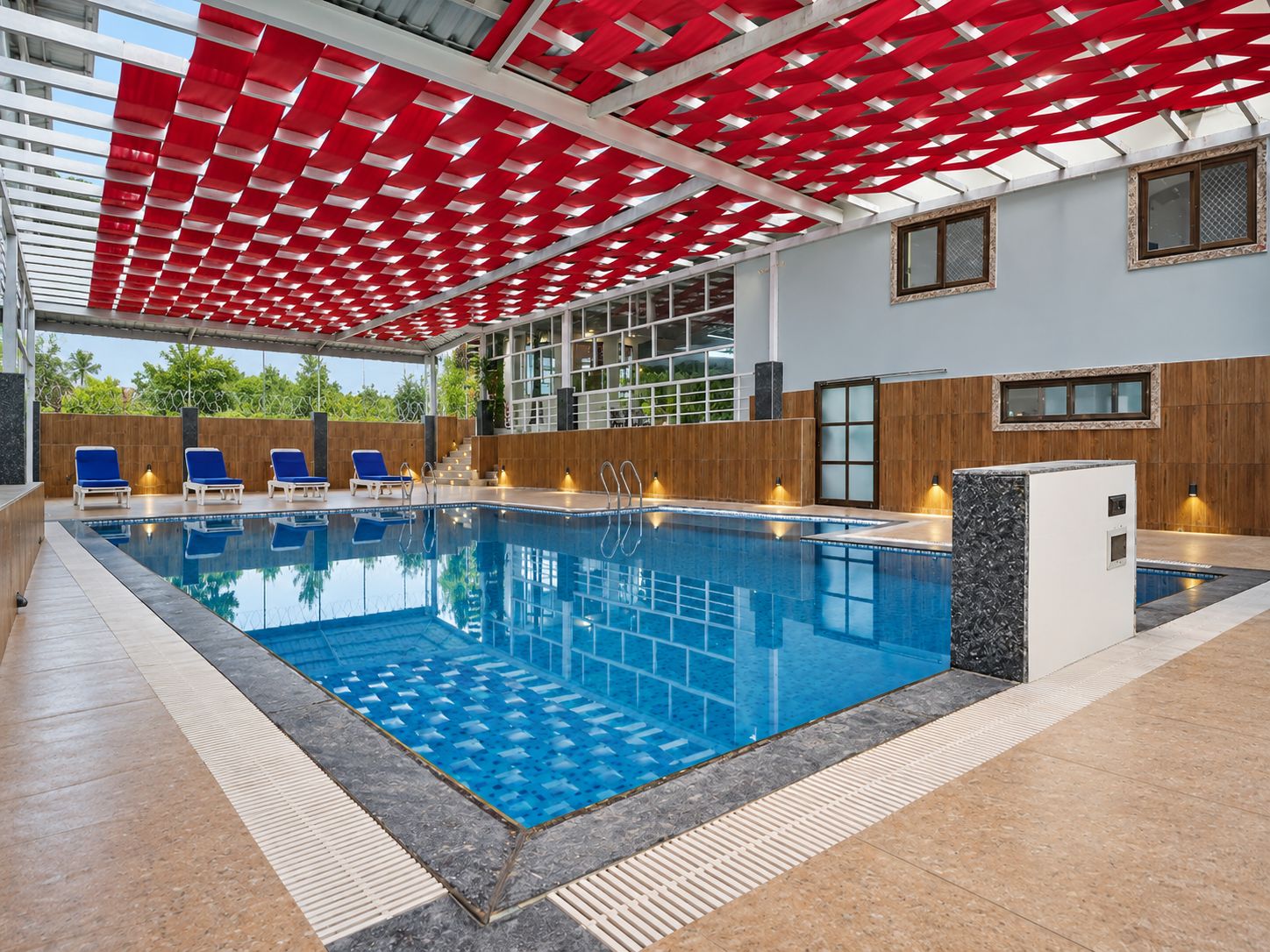 Una piscina interior con azulejos azules, rodeada de sillones de descanso y una pared de madera.