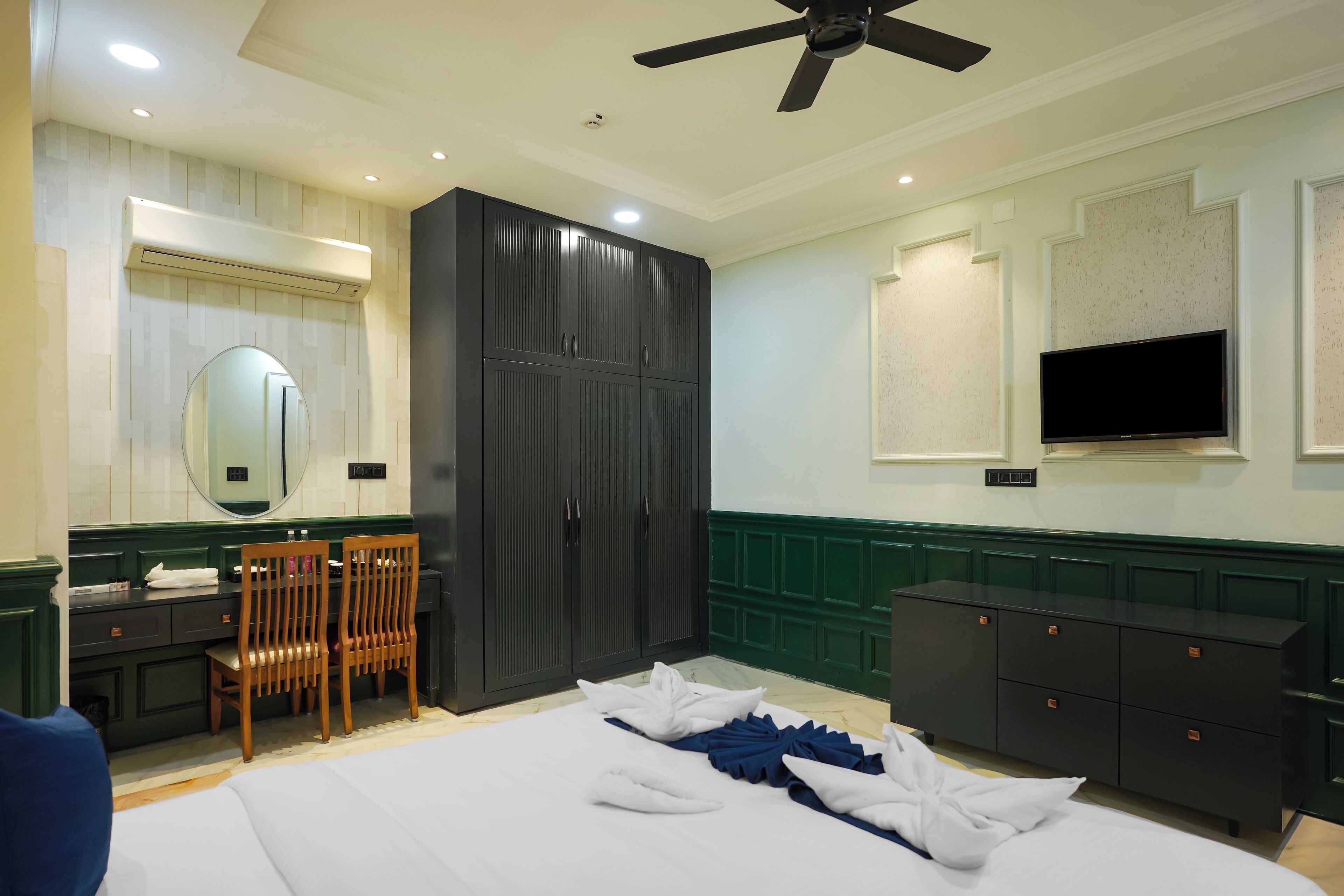 Habitación de hotel con cama, escritorio, armario, espejo y televisión.