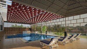 An indoor swimming pool with clear glass walls, a tiled floor, and sun loungers. - The Forest Hills Resort (Sarada)